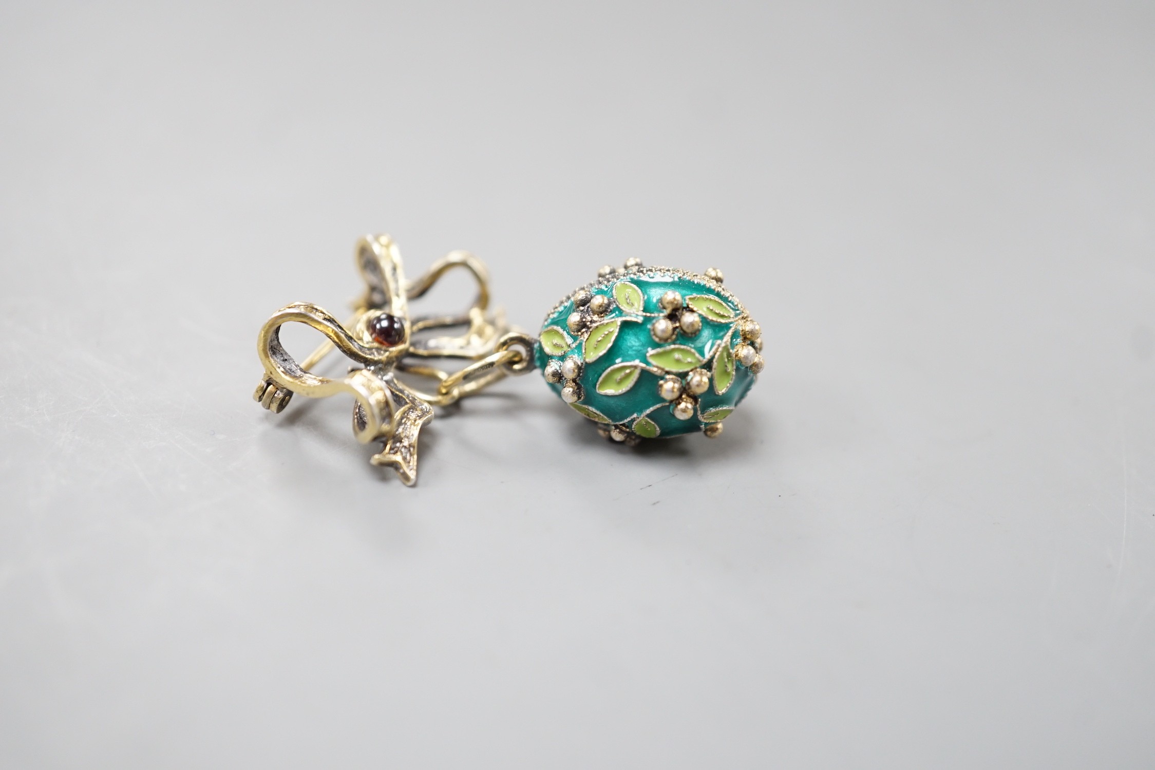 A mid 20th century Soviet gilt 925 and enamelled egg pendant, 21mm, on a gilt white metal ribbon bow suspension brooch.